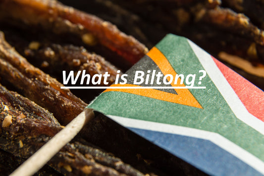 "What is Biltong" is written in white text across a photo of a South African flag laying on some biltong steaks